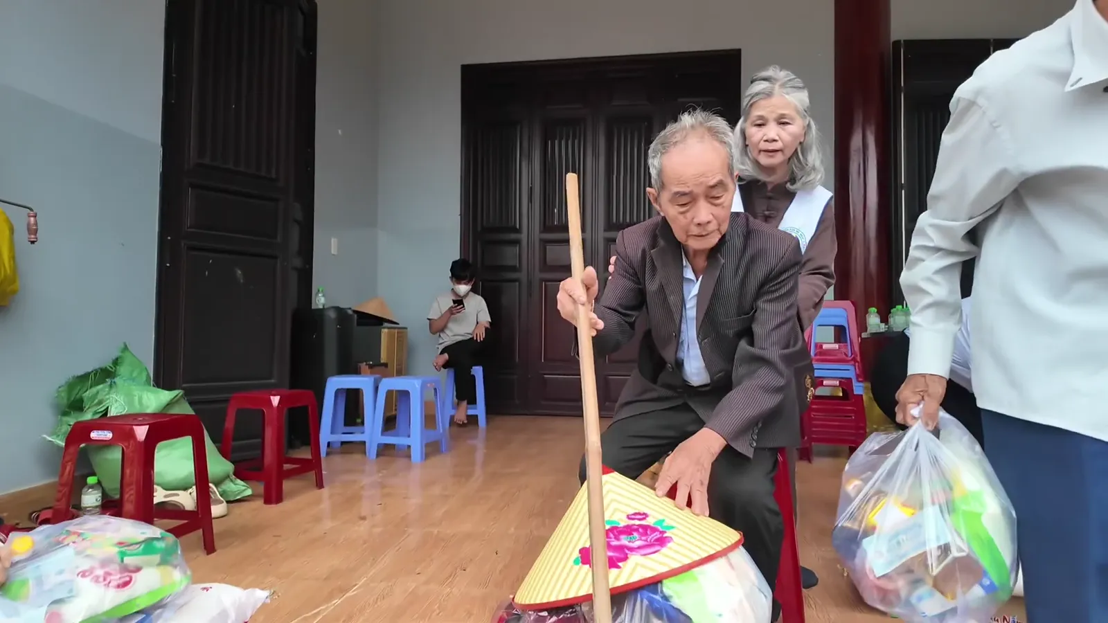 An elderly man leaning on a stick receives a gift bag at Phước Huệ Pagoda, Đà Nẵng